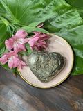 pyrite heart on a pink plate by pink flowers on a green leaf on a wooden table