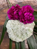 a light Green Apophyllite crystal by pink carnations on a green leaf in a wooden bowl