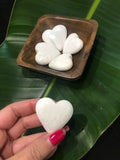 white scolecite crystal hearts in a wooden bowl and one being held in front of a dark green leaf