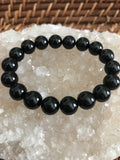 10 mm bead black tourmaline crystal  bracelet on a white apophyllite crystal on a wicker tray