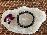 10 mm bead black tourmaline crystal stretch bracelet near a maroon orchid flower on a white apophyllite crystal on a wicker tray