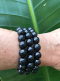three black bead shungite crystal bracelets on a woman's arm in front of a dark green leaf