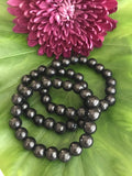 three black bead shungite crystal bracelets laying on a green leaf with a maroon chrysanthemum flower by it