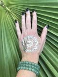 three light green aventurine crystal bead bracelets on a woman's arm with a gold tattoo on her hand black fingernails against a green palm leaf