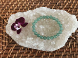 light green aventurine crystal bead bracelet by a maroon orchid flower on a white apophyllite crystal on a wicker tray