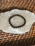 a dark brown bronzite bead crystal stretch bracelet on a white apophyllite crystal on a wicker tray