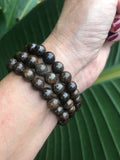 three brown bronzite crystal bead bracelets on a woman's arm against a dark green leaf