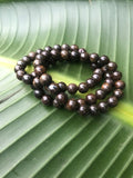 three bronzite crystal bead bracelets stacked on top of a green heliconia leaf