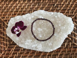 a garnet faceted crystal stretch bracelet near a maroon orchid flower on a white apophyllite crystal on a wicker tray