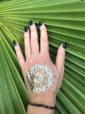 a dark red garnet faceted crystal stretch bracelet on a woman's arm with a gold press on tattoo on her hand with black nails against a green palm leaf