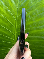 Teardrop-shaped black and white agate crystal flame held in a hand with a green leafy background - 2