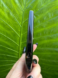 Teardrop-shaped black and white agate crystal flame held in a hand with a green leafy background - 2
