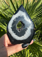 Teardrop-shaped black and white agate crystal flame held in a hand with a green leafy background-4