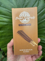 Huma Sagrado incense stick packaging held in front of green leaves