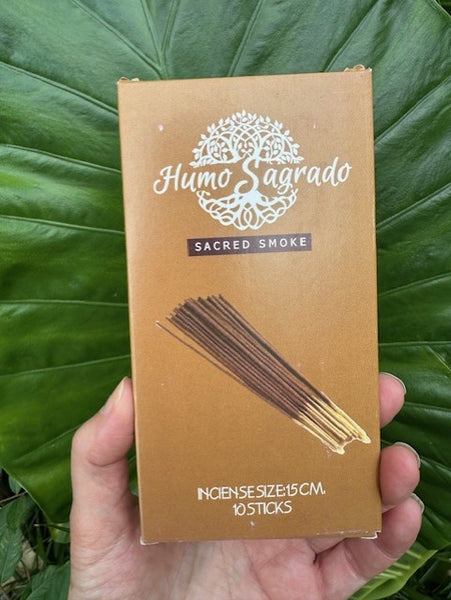 Huma Sagrado incense stick packaging held in front of green leaves