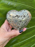 pyrite heart held by a woman's hand in front of a large green leaf