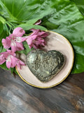 pyrite heart on a pink plate with pink flowers on a green leaf on a wooden table