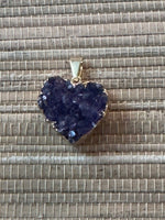 a dark purple heart shaped amethyst with gold pendant on a natural fiber tan background