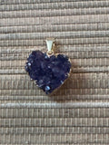 a dark purple heart shaped amethyst with gold pendant on a natural fiber tan background