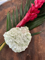 a light Green Apophyllite Crystal by a red ginger flower with green leaf in a wooden bowl