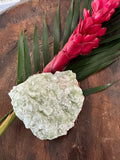 a light Green Apophyllite Crystal by a red ginger flower with green leaf in a wooden bowl