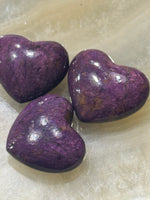 a group of three purple and golden sheen Purpurite crystal heart on a white plate