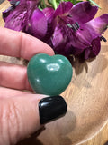 a woman holding a small green aventurine crystal heart by a pink flower over a wooden tray