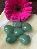 a group of several small green aventurine crystal hearts in front of deep pink gerbera daisy on a white plate