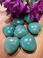 a group of small green aventurine crystal hearts by a purple flower on a wooden plate