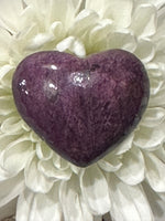 a close up of a purple and light sheen Purpurite crystal heart in the middle of a white flower