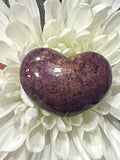 a small purple and gold sheen Purpurite crystal heart in a white flower turned slightly to the right