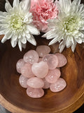 a bowl of pink rose quartz crystal hearts in a wooden bowl with white and pink flowers