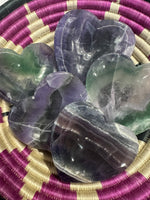 several dark purple and green rainbow fluorite heart dishes in a hot pink, white and black woven bowl