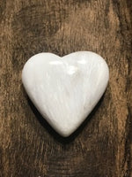 Heart shaped white scolecite crystal heart on a wooden plate
