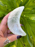 person holding a white selenite half moon dish against a green leaf background