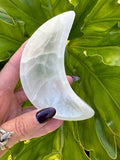 person holding a white crescent half moon selenite dish against a green leaf background