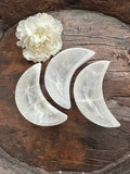 3 selenite white half moon dishes against a wood background and a white flower