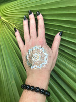 10 mm black tourmaline crystal stretch bracelet on a woman's arm with a gold press on tattoo with black nails against a green palm leaf
