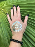 10 mm black tourmaline crystal stretch bracelet on a woman's arm with a gold press on tattoo with black nails against a green palm leaf