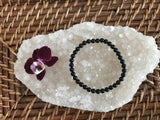4 mm bead black tourmaline crystal stretch bracelet by a maroon orchid flower on a white apophyllite crystal on a wicker tray