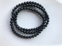 three 4 mm bead black tourmaline crystal stretch bracelets against a white background