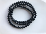 three 4 mm bead black tourmaline crystal stretch bracelets against a white background