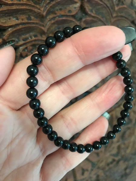 4 mm bead black tourmaline crystal stretch bracelet being held by a woman against a dark indian carved wooden board