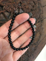 4 mm bead black tourmaline crystal stretch bracelet being held by a woman against an indian carved wooden board