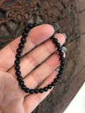 4 mm bead black tourmaline crystal stretch bracelet being held by a woman against an indian carved wooden board