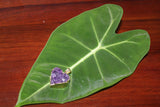 a raw purple heart shaped pendant that is gold plated on a green heart shaped leaf on a brown table