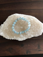 a light blue aquamarine crystal bracelet on a white apophyllite crystal on a wood board