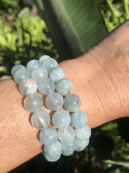 three light blue aquamarine crystal  bracelets on a woman's arm against a green leafy background