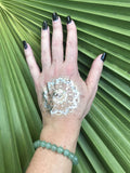 light green aventurine crystal bead bracelet on a woman's arm with a gold tattoo on her hand black fingernails against a green palm leaf