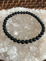 black tourmaline crystal stretch bracelet on top of a white apophyllite crystal on a wicker tray